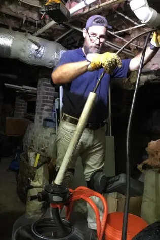 Crew Plumbing plumber clearing a drain with a drain snake in a basement