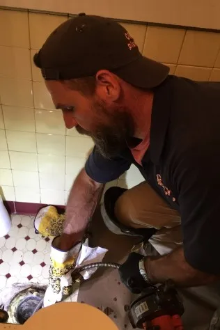 Crew Plumbing plumber using a drain cleaning machine on a bathroom floor drain