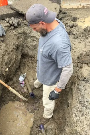 Kevin Tidwell standing in a dug-out trench next to an underground pipe