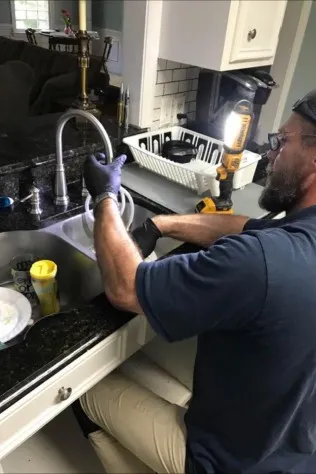 Crew Plumbing plumber working on a kitchen sink and faucet