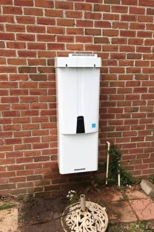 Finished tankless water heater installation on an exterior brick wall